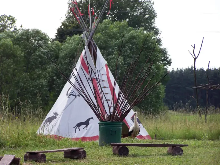 Wioska indiańska na Mazurach z tipi ozdobionym zwierzętami, bocianem i łukami.